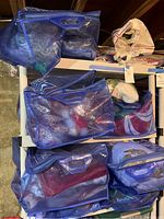 Blue mesh storage bags containing assorted holiday decorations for various holidays, stacked on a shelving unit in a basement.