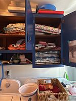 Wooden storage cabinets above washer and dryer filled with various folded kitchen linens and towels