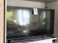 Front view of LG flat screen TV on surface with note attached, showing size and reflective screen.