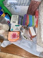 Photo showing assorted soaps, sponges, cleaning liquids, and bath mats next to striped fabric basket and rolled-up shower curtain.