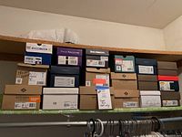 Wide shot of multiple stacked shoe boxes arranged in two rows on a shelf, showing a variety of brands and sizes mainly size 8, including handwritten tags and labeled boxes