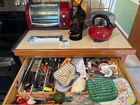 Photo of toaster oven, tea kettle on countertop and open drawer with knives and utensils inside.
