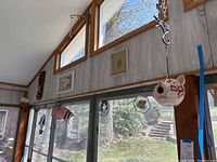 Wide shot of sunroom wall with hanging ceramic cat face wind chime, geometric glass shapes, stained glass cat suncatcher, and framed artwork above.