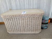 Side view of white wicker storage bench with wooden top and part of marble-patterned pedal bin visible behind