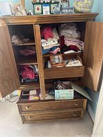 Opened wooden cabinet showing folded women's clothing and some accessories.