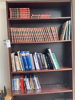 Full view of a wooden bookshelf with multiple shelves holding encyclopedias, assorted books, and DVDs.