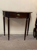 Front view of the demi lune table showing the curved shape and central drawer with brass hardware.