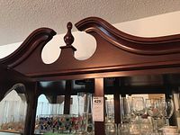 Shelf with assorted glass stemware including wine glasses, tall and short branded glasses, and demitasse cups inside wooden cabinet