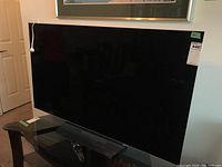 Front view of TV on glass stand with remote control on shelf, power cable draped