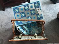 Overhead view inside wicker picnic basket showing melamine plates, acrylic glasses, and placemats.