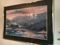 Framed landscape print in metal frame, showing mountain and river scene with muted colors