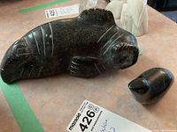 Pair of soapstone animal carvings on display from angled top view, showing details of the dark polished surface and carved lines.