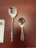 Two sterling silver spoons on wood surface showing front view, one baby spoon and one soup spoon