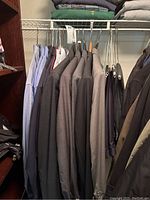 Multiple dark and neutral colored men's suits hanging in a closet on hangers.