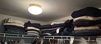 Shelf with multiple stacks of folded men's sweatshirts and sweaters in size medium to large, various colors, some vintage with Atlanta 1996 embroidery.