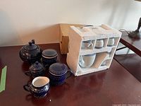Blue polka dot ceramic teapot with lid, creamer, sugar bowl with lid, two lidded mugs arranged on table