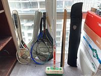 Photo showing rackets, curling sweeper, and pool cue with case by a window.