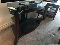 Side angle view showing the curved front wood legs and clear glass top shelf with black tinted lower shelves.