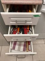 Photo of three partially opened drawers showing kitchen utensils, towels and cutlery, highlighting the content variety.