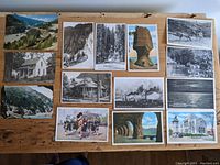 All 14 postcards laid out on wooden surface, front sides visible showing various landscapes, buildings, natural formations, and cultural images.