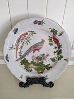 Front view of one vintage hand painted decorative plate depicting three colorful birds surrounded by flowers and butterflies with a gold rim and crackle glaze.