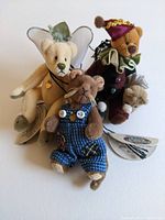 Full view of three miniature stuffed animals with movable limbs, showing white teddy bear with fairy wings, brown teddy bear in jester costume, and mouse in blue overalls.