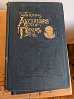Front cover of one volume showing title 'Works of Alexandre Dumas' with embossed silhouette and decorative details.