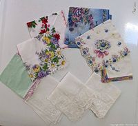 Nine vintage and antique handkerchiefs displayed overlapping, showing floral prints, lace, and embroidery in various colors and styles.
