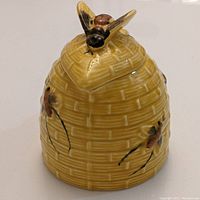 Front view of yellow ceramic honey pot showing basket weave pattern and bee figurine lid handle