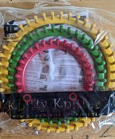 Three circular Knifty Knitter looms in yellow, green, and pink with instruction sheets inside a plastic bag.