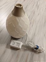 White ceramic essential oil diffuser with patterned surface and beige top, showing power adapter.