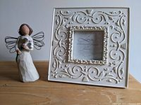 Front view of Susan Lordi angel figurine standing next to the decorative photo frame on a wooden surface.