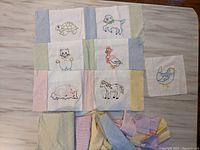 Top view of quilt project with 7 finished embroidered animal squares arranged in 3 rows and several coordinating fabric remnants beneath.