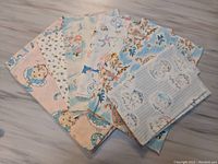 Lot of seven fabric remnants spread out, showing various baby-themed and floral prints in pastel colors.