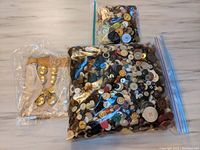 Photo showing two zippered plastic bags filled with a variety of loose vintage buttons and a card with gold-tone buttons attached.
