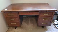 Full frontal view of the solid wood desk showing all drawers and brass handles.