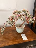 Overall view of the artificial bonsai tree with pink, white flowers and orange berries in a white ceramic pot on a wooden surface.