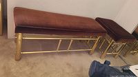 Side view of two brass benches with brown cushioned tops, placed on carpeted floor against wall.
