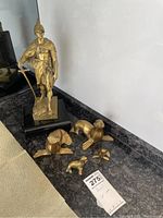 Overview of the brass Roman soldier statue alongside four smaller brass seal figurines on a countertop with a price tag visible.