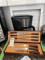 Photo of carving set containing knives with wooden handles, carving fork, and a blade sharpener inside a brown lined wooden case