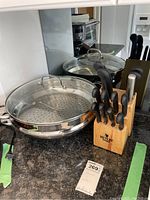 Photo showing circular stainless steel Cuisinart steamer with perforated base and glass lid next to a wooden block of knives.