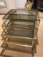 Photo showing the three brass colored metal and glass nesting side tables stacked together, highlighting their size difference and structure.