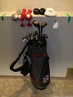 Full view of TaylorMade golf bag filled with various clubs and placed against a wall, showing headcovers on top of the bag.