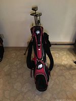Front view of the red and black Sun Mountain B golf bag with golf clubs inside.
