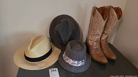 Three hats and one pair of Dan Post cowboy boots displayed on a surface against a wall.