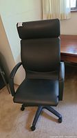 Front view of black Ikea office chair with padded seat, backrest, headrest, armrests, placed next to a wooden desk.