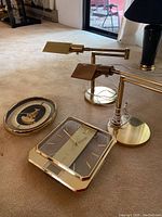 Photo showing two brass-colored adjustable desk lamps and two brass-colored wall clocks on carpet