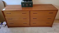 Front view of the full dresser showing all six drawers and top surface with a decorative safe placed on top.