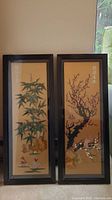 Two full framed stone art panels with Asian themes side-by-side on carpeted floor in front of window.