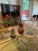 Wide view showing three vases on a glass table in front of a TV and sliding glass door.